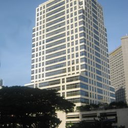 6750 Ayala Avenue is a tall white building with multiple windows under a clear blue sky. Taken while riding a bus traversing the side of Ayala Avenue opposite that of Landmark and Glorietta.