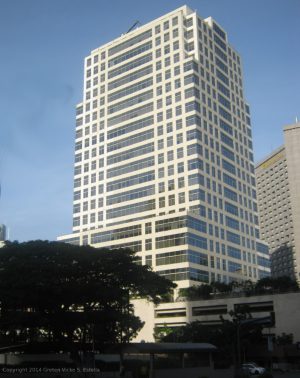 6750 Ayala Avenue is a tall white building with multiple windows under a clear blue sky. Taken while riding a bus traversing the side of Ayala Avenue opposite that of Landmark and Glorietta.