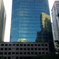 The tower of 88 Corporate Center has a facade made of blue glasses that forms a fork on the top. In the middle of the fork is a part of the building that has a concrete facade with small square windows. The lower levels of 88 Corporate Center on the side shown here is a podium structure on which the tower is mounted. The podium levels have several rectangular windows that seem to be open-air indicative of a parking level. However, the glass facade of the tower extends to the right side of the lower levels, and is partly seen in this picture.