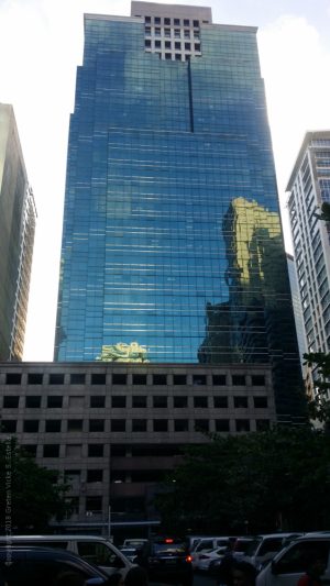 The tower of 88 Corporate Center has a facade made of blue glasses that forms a fork on the top. In the middle of the fork is a part of the building that has a concrete facade with small square windows. The lower levels of 88 Corporate Center on the side shown here is a podium structure on which the tower is mounted. The podium levels have several rectangular windows that seem to be open-air indicative of a parking level. However, the glass facade of the tower extends to the right side of the lower levels, and is partly seen in this picture.