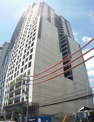 A vertical panorama of Annapolis Wilshire Plaza as seen from the sidewalk on the other side of Annapolis St. near its intersection with Columbia St. Its facade is white concrete with many square windows.