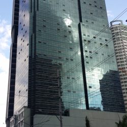 Antel Global Corporate Center is a tall cuboid structure with a lower podium of a teal concrete exterior at about one-fourth of its height and upper levels of a teal glass facade. This is the building as seen from Garnet Road corner Julia Vargas Ave.