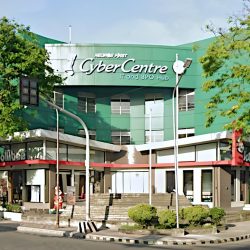 Negros First Cyber Centre, a three-story low-rise building with mostly green facade as seen from the opposite corner of Hernaez and Lacson. The ground floor of the building is now occupied by a branch of Jollibee fastfood.