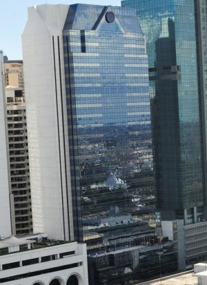 BPI Buendia Center has a tall rectangular prism shape with a trapezoidal prism on top. It features a concrete facade on the side face and a front face covered in dark glass panels. This picture was taken from the fifteenth floor of Citadel Inn Makati.