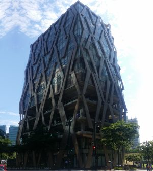 The floors of Clipp Center have an exterior covered with large transparent glass panels on the two lowest stories, open verandas for parking on the next three levels, and dark glass panels on the upper floors, all overlayed by diamond-shaped steel patterns. This is Clipp Center, as seen from the open parking area of KFC on the opposite corner.