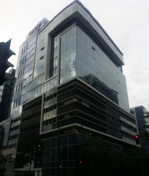 The Cocolight Building is a blocked-shaped midrise building. It has a glass surface and some white concrete highlights. The lower levels have darker glass panels or no glass at all, possibly parking areas. The upper parts have bluish glass panels. As seen from the side, the glass panels and white concrete lining seems to form a square bracket with extended top, and a short vertical rectangle in front of it, with the extended part of the bracket above the rectangle. The holes between the bracket and the rectangle are recessed sections of the wall. As seen in front, the blue glasses are continuous with a horizontal recess on second to the top floor.