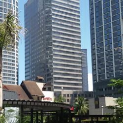 CyberOne Building, as seen from along the Orchard Road near its southern end that intersects with Eastwood Avenue. CybeOne is a gray high-rise building with alternating horizontal bands of concrete and glass windows. Decorative letters forming MEGAWORLD is near its top, just above the topmost glass row.