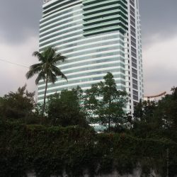 The Cyberpark Tower 2 is rectangular with bulging front and back surfaces and a green facade. This picture was taken from EDSA cor. Tuazon Boulevard. A white wall with plants crawling on it obscures the lower levels of Cyberpark Tower 2.