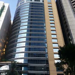 The right side of the Discovery Centre has a yellow concrete facade with small square windows, while the left is a quarter cylindrical structure covered in glasses. This is the view from across ADB Avenue in front of The Podium.