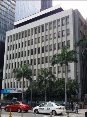 The Emerald Building is a low-rise blocky building with a facade of rows of small rectangular glass windows surrounded by gray concrete walls.