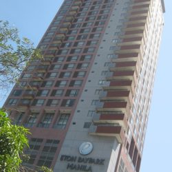 Eton Baypark Manila has a vertical rectangular prism structure, red and gray colors, and windows of either glass panels or steel railings. The building was photographed from the opposite side of Kalaw St.
