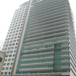 Gateway Tower is a gray rectangular prism with a concrete and glass facade and uneven divide. The larger part has bands of gray concrete and green glass panels, while the smaller part has small square windows. The photo was taken from the sidewalk along Gen. Malvar Ave. near Cambridge St.