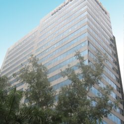 Global One Center is a tall cuboid structure with an exterior of alternating bands of glass panels and gray concrete. This is the building, as seen from the segment of Eastwood Palm Tree Ave. between E-commerce and Citywalk 1.