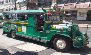 A green jeepney is shot at angle where you can see most of its right side and some of its front. The signage on the side on a yellow background read as: Greenhills Shopping Center, Florida Missouri via Connecticut Unimart, Annapolis, MRT, Gate-5. There are also labels GSC JODA - Greenhills Shopping Center Jeepney Operator's Driver's Association (sic) and Lawin Motors on the side under the yellow signage. The signage in front also on yellow background read as: Greenhills Shopping Center, Annapolis, Gate-5. There's also a big sign Mary Mediatrix above the driver's viewing window.