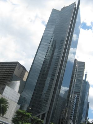 GT Tower has an angular design with sharp angles and diagonal patterns. Its exterior is covered in blue glass panels, and the top has triangular fins, giving it an obelisk-like appearance. Photo taken from the sidewalk at the corner of Ayala Avenue and Amorsolo St.