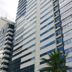 Hanston Square has a blocky structure and an exterior of dark glass and white concrete. The view from the sidewalk on the opposite side of San Miguel Ave. and adjacent to Lourdes School is shown here.