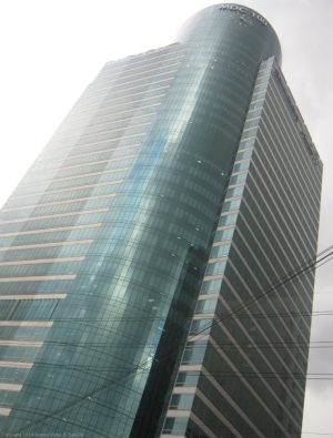 MDC 100 is a cuboid structure with a cylinder inserted in one corner. The cuboid has alternating rows of concrete and glass, while the cylinder's facade is all glass panels. The picture was taken from the lower staircase levels on the other side of E. Rodriguez Ave. The staircase is the access to the footbridge connecting both sides of E. Rodriguez.