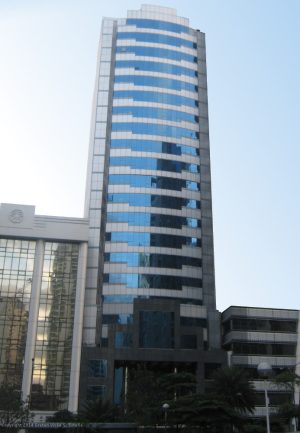 Multinational Bancorporation Centre is a tall rectangular prism with a facade of alternating bands of gray tiles and dark glasses on the upper floors and black tiles on the lower floors. The picture was taken from within the car park along Ayala Avenue on the opposite side. The adjacent LKG tower was edited to make Multinational Bancorporation Centre stand out.