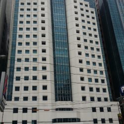 The exterior of the Octagon Center is white concrete with several small square windows and a continuous section of vertical glass panels in the middle. This picture was taken from the Petron gasoline station across San Miguel Ave.