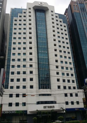 The exterior of the Octagon Center is white concrete with several small square windows and a continuous section of vertical glass panels in the middle. This picture was taken from the Petron gasoline station across San Miguel Ave.