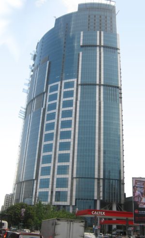 One Corporate Center has a facade of various sizes of blue glass panels and a roof that spirals upward. This photograph was taken from the open park under the flyover along Meralco Ave., north of Julia Vargas Ave.