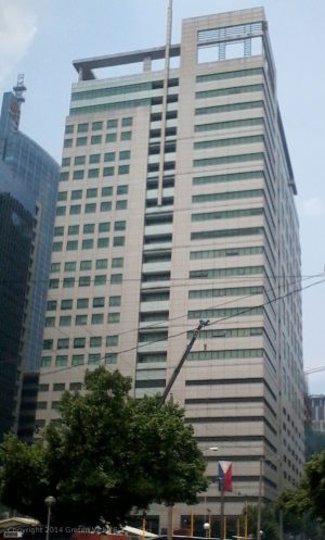 Solaris One is a tall, modern high-rise with light-colored external walls and green sections. Its windows are rectangular, arranged in a grid pattern, creating a symmetrical facade. An overhang structure at the top adds depth, while an additional structure extends above the roofline, featuring vertical lines and open spaces. This contrast to the grid-like pattern on the main body creates a visually interesting element. The building’s design caters to the needs of modern businesses. This is Solaris One as seen from sidewalk at Dela Rosa cor. Sotto St.