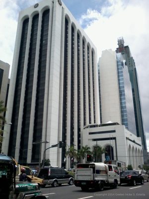 Busy street with cars in front of tall, modern buildings under a partly cloudy sky. Pacific Star building, the one in front, as seen from front of RCBC Makati Ave. branch (Makati Ave. cor Buendia). The buildings BPI Buendia Center and Petron Megaplaza (right) and BDO Corporate Center (left).