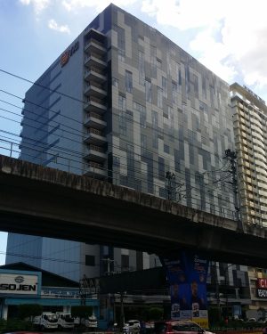 Panorama TechnoCenter is a cuboid building with patterns of gray and white Tetris blocks. Shown here is the view from across EDSA. The LRT rail structure partially blocks th building.