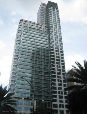 High-rise building with glass facade and red logo at the top, flanked by palm trees.