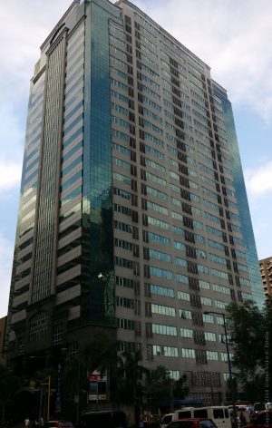 The Prestige Tower is a tall rectangular prism with an exterior of gray concrete, dark green glass panels, and dark gray marble near the entrance. This is the building, as seen from the sidewalk on the opposite side of Emerald in front of the Orient Square.