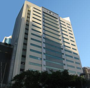 The facade of PSBank Center is predominantly composed of white concrete, interspersed with narrow strips of glass windows on each level. This view is from Paseo De Roxas cor. Ayala Ave. on the sidewalk adjacent to Ayala Tower One.
