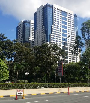The Tektite Towers is a building made of two cuboid towers with a facade of white concrete and blue glass panels. The picture was taken from the sidewalk along San Miguel Avenue between Julia Vargas Ave. and the main gate of the San Miguel compound.