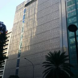 Security Bank Centre's exterior is white and covered by intricate patterns. One side has a column of visible blue glass panels. This picture is as seen from the other side of Ayala Avenue in front of Alphaland Tower.