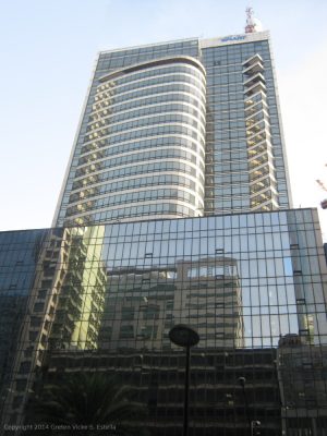 Smart Tower has a facade of glass panels in its entirety. The structure can be divided into the podium and the tower. The cuboid podium covers the entire land area, while the tower has smaller floor areas and is recessed from the frontage. This is Smart Tower seen with the camera slanted upward while standing on the sidewalk on the opposite side of Ayala Avenue between Rufino Pacific Tower and Makati Sky Plaza.