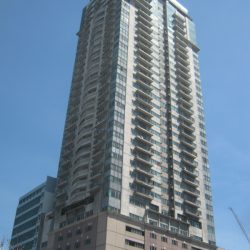 Sunview Palace is a tall rectangular prism with a cylindrical structure on top. Its colors are white and light maroon, and it has several windows and balconies. This is the view from the other side of Kalaw St., approximately where the opposite corner will be situated should Del Pilar St. extend beyond the intersection.