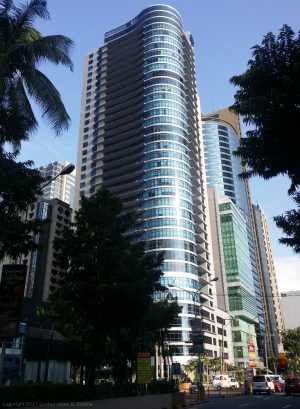 The Malayan plaza has a blue glass exterior. It has a tall block shape with an overlapping cylinder in one corner.