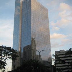 Reflective blocky skyscraper Zuellig building under a partly cloudy sky as seen from the sidewalk at Paseo De Roxas cor. Villar St. adjacent to Citibank Center.